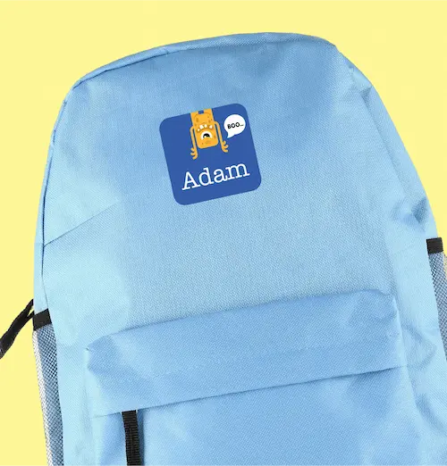 Light blue backpack featuring a playful sticker with an orange cartoon monster saying "Boo" and the name "Adam Smith" underneath, creating a whimsical tone.